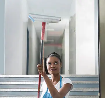 A woman holding a mop in front of stairs.