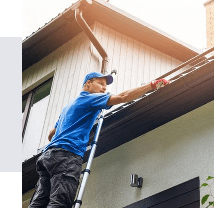 A man on a ladder cleaning the roof of a house.