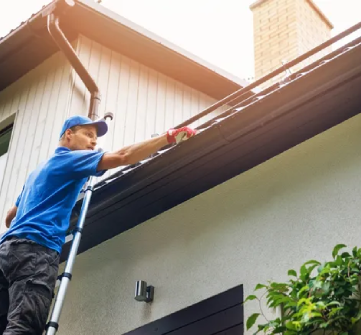 A man on a ladder cleaning the gutter of his house.